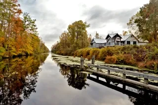 Calm swamp surrounded by bright fall foliage and visitors center on cloudy day.