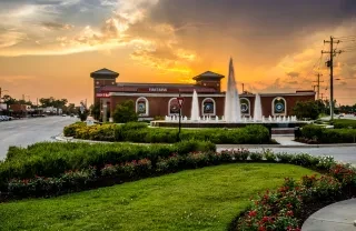 Freedom Fountain surrounded by gardens as sun sets behind building in distance.