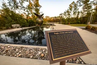 Eagle, Globe and Anchor plaque in foreground with memorial in background at Lejeune Memorial Gardens.