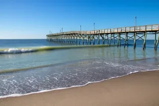 Holden Beach Pier jutting into water during daytime in NC's Brunswick Islands.