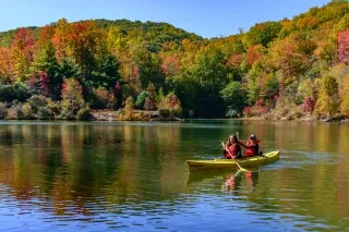Two friends kayaking in calm lake surrounded by bright fall foliage.