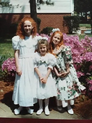 Three sisters in dresses standing in front of pink blooming flowers.