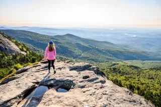 Woman walking on Macrae Peak Lookout at Grandfather Mountain with stunning vistas in distance.