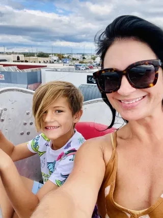 Woman smiling with son while riding Ferris wheel with boats in background during daytime.