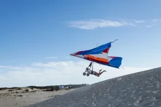 Person hang gliding over sand dunes during daytime.