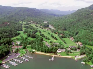 Aerial of Rumbling Bald golf courses surrounded by trees and mountains in background.