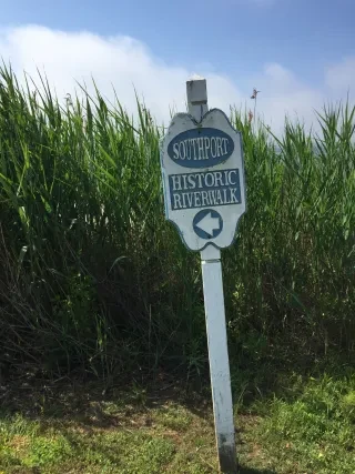 Sign reading Southport Historic Riverwalk in front of tall green grass.