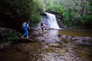 Couple hiking at base of waterfall in Jackson County on summer day.