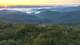 Aerial view of tower in middle of trees and mountains with sun rising in background