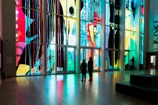 Two friends admiring large stained glass wall in museum.