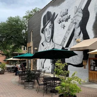 Earl Scruggs mural on side of Newgrass Brewing Co. with tables and umbrellas in front.