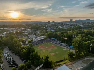 Aerial of McCormick Field at sunset in downtown Asheville with mountains in background.