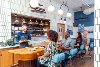 Four people sitting at bar in Seabird restaurant with waiter serving food.