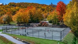 People playing tennis on courts with mountains and fall foliage in background.