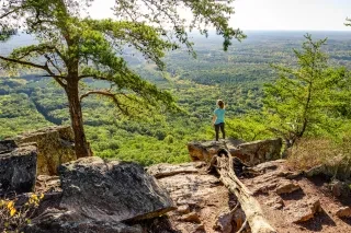 A woman stands at the edge of a cliff overlooking a valley at the top of Crowders Mountain.