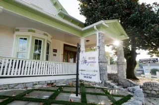 Exterior of Magnolia House Motel with signs and tree in front year.