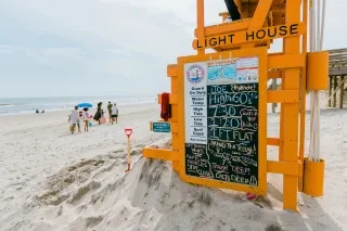 Orange lifeguard stand with family walking on sand and ocean to the left.
