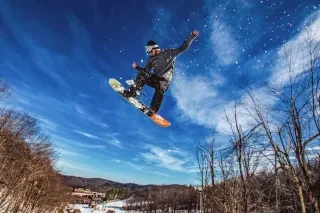 Snowboarder in midair after making jump with snow flying behind him