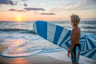 Professional surfer Tony Silvagni gazing out into ocean while holding a surfboard.